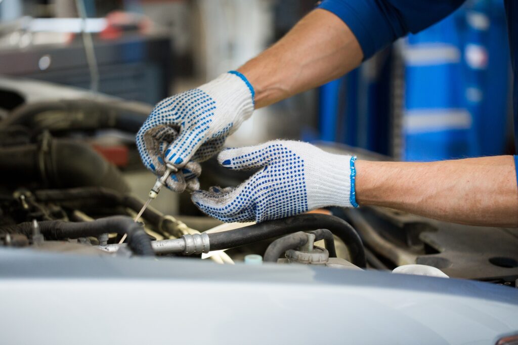 mechanic with dipstick checking motor oil level